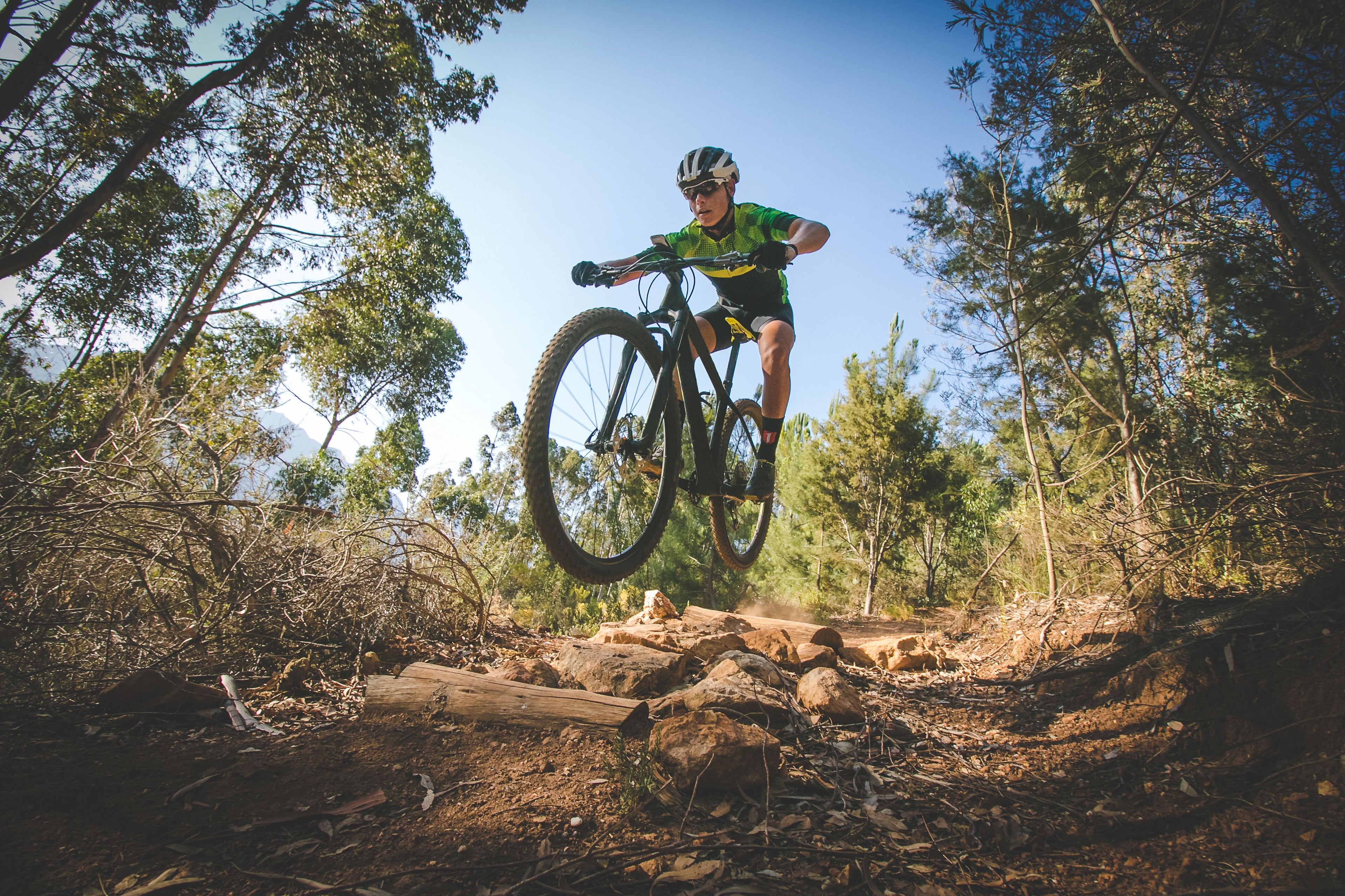 Biker in mid-air over a log on a forest trail
