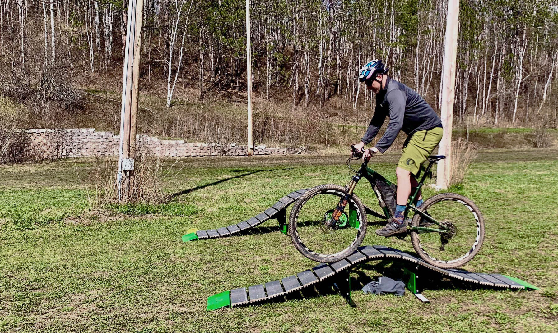 Person riding a bike over a small ramp in an outdoor setting with trees in the background